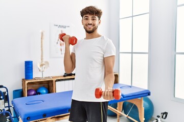 Young arab man patient doing rehab using dummbells at clinic