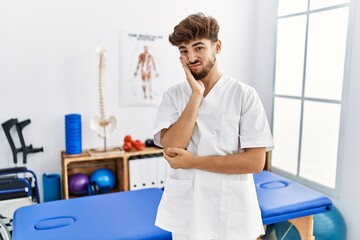 Fototapeta premium Young arab man working at pain recovery clinic thinking looking tired and bored with depression problems with crossed arms.