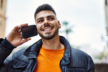 Handsome hispanic man with beard smiling happy and confident at the city wearing winter coat...