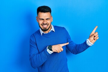 Young hispanic man with beard wearing casual blue sweater pointing aside worried and nervous with...