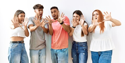 Group of young friends standing together over isolated background afraid and terrified with fear expression stop gesture with hands, shouting in shock. panic concept.