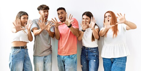 Obraz premium Group of young friends standing together over isolated background afraid and terrified with fear expression stop gesture with hands, shouting in shock. panic concept.