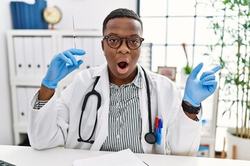 Young african doctor man holding syringe at the hospital surprised pointing with finger to the side, open mouth amazed expression.