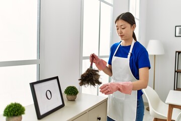 Young chinese housewife cleaning dust using duster at home.