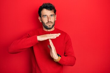 Handsome man with beard wearing casual red sweater doing time out gesture with hands, frustrated...
