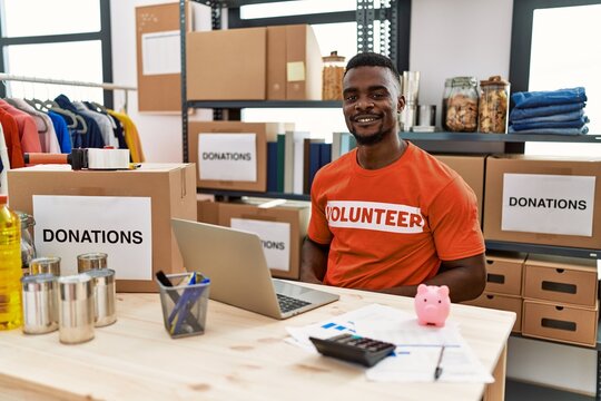 Young african man working as volunteer t shirt at donations stand looking positive and happy standing and smiling with a confident smile showing teeth