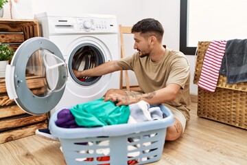 Young hispanic man smilig confident using washing machine at laundry room