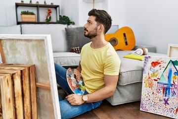 Young man with beard painting canvas at home looking to side, relax profile pose with natural face...