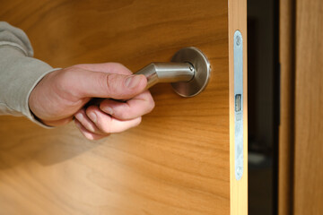 A man's hand opens the wooden door of a house or apartment. Close-up of a doorknob