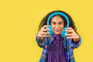 hermosa mujer afroamericana viendo a cámara en fondo amarillo con audífonos en la mano