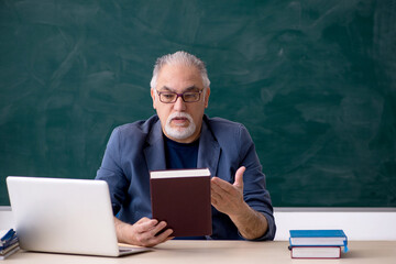 Old male teacher holding book in the classroom