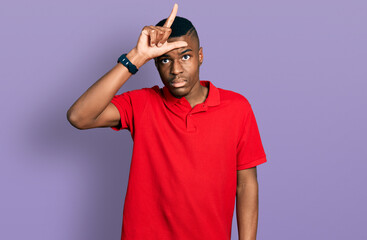 Young african american man wearing casual red t shirt making fun of people with fingers on forehead doing loser gesture mocking and insulting.