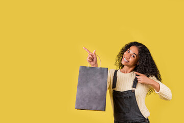 mujer señalando a un lado con bolsas de compra en estudio con fondo amarillo