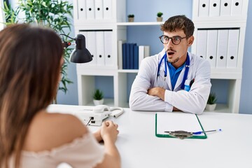 Young doctor with client at medical clinic afraid and shocked with surprise expression, fear and excited face.