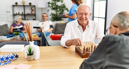 Two retired man smiling happy playing chess at nurse home.