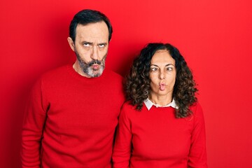 Middle age couple of hispanic woman and man hugging and standing together making fish face with lips, crazy and comical gesture. funny expression.