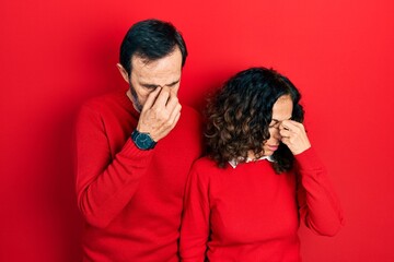 Middle age couple of hispanic woman and man hugging and standing together tired rubbing nose and eyes feeling fatigue and headache. stress and frustration concept.