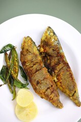 Indian Mackerel fish fry. Bangda Rava fry. whole Fried fish served on a banana leaf with fried chilies, lemon slices, and Indian spices. also known as talalele bangde in Marathi. Copy space.