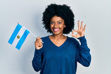 Young african american woman holding argentina flag doing ok sign with fingers, smiling friendly gesturing excellent symbol