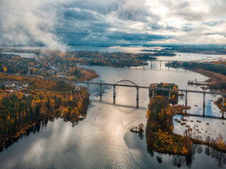 Aerial photo of old railway suspension bridge above river. Autumn landscape with northern nature. Trees with yellow and orange leaves on background. Cloudy sky. Transportation concept.