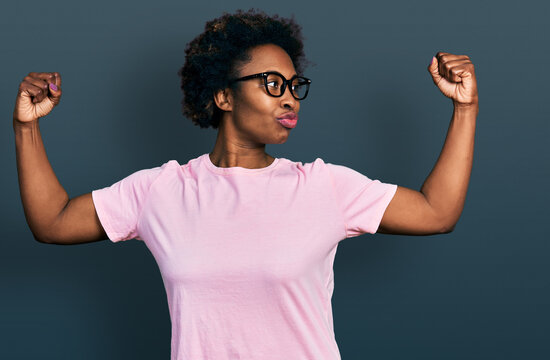African american woman with afro hair wearing casual clothes and glasses showing arms muscles smiling proud. fitness concept.