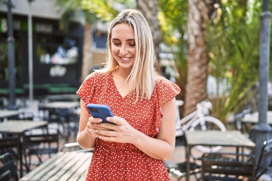 Young blonde girl smiling happy using smartphone at the city.