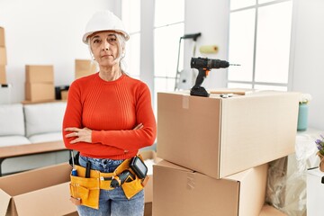 Middle age grey-haired woman wearing hardhat standing at new home relaxed with serious expression on face. simple and natural looking at the camera.