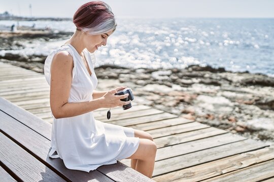 Young caucasian girl using professional camera sitting on the bench at the beach.