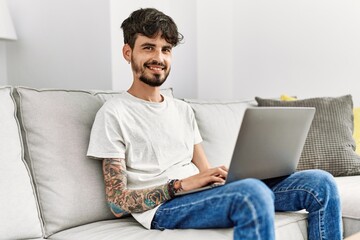 Young hispanic man using laptop sitting on the sofa at home.