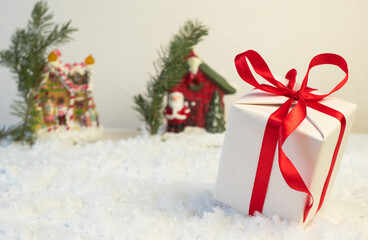 Obraz na płótnie Canvas Volgograd, Russia - October 15, 2021: A gift box with a red ribbon lies on the snow. Christmas or New Year's gifts on the background of a snow-covered road, in the background houses and Christmas