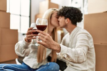 Young beautiful couple kissing and toasting with red wine at new home