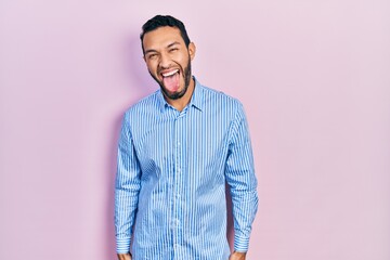 Hispanic man with beard wearing casual blue shirt sticking tongue out happy with funny expression. emotion concept.