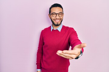 Hispanic man with beard wearing business shirt and glasses smiling cheerful offering palm hand giving assistance and acceptance.