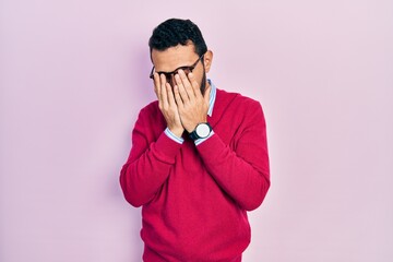 Hispanic man with beard wearing business shirt and glasses with sad expression covering face with hands while crying. depression concept.