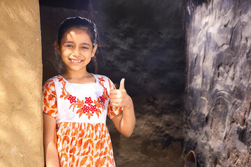 Happy rural Indian girl child standing on the cottage threshold in an Indian village outside her...