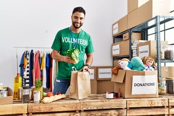 Young arab man wearing volunteer uniform preparing groceries paper bag at charity center