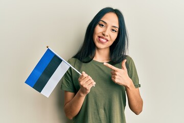 Fototapeta premium Young hispanic girl holding estonia flag smiling happy pointing with hand and finger