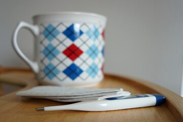 Cup of tea with a checkered pattern, paper handkerchiefs and a personal thermometer on a wooden table