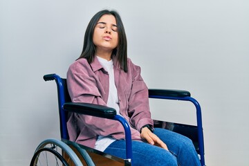 Young brunette woman sitting on wheelchair looking at the camera blowing a kiss on air being lovely and sexy. love expression.