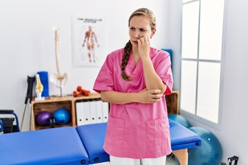 Young blonde woman working at pain recovery clinic looking stressed and nervous with hands on mouth biting nails. anxiety problem.