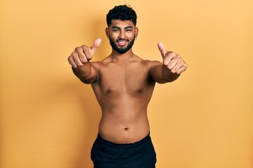 Fototapeta premium Arab man with beard wearing swimwear shirtless approving doing positive gesture with hand, thumbs up smiling and happy for success. winner gesture.