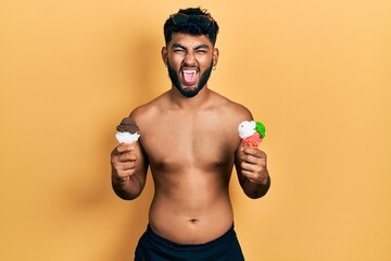 Fototapeta premium Arab man with beard wearing swimwear eating two ice cream cones sticking tongue out happy with funny expression.