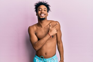 Fototapeta premium Young african american man with beard wearing swimsuit cheerful with a smile of face pointing with hand and finger up to the side with happy and natural expression on face
