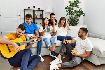 Group of young friends on party smiling happy and playing classical guitar at home.