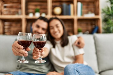 Young latin couple smiling happy toasting with red wine glass at home.
