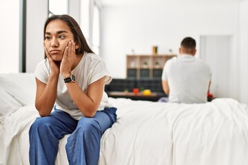 Young latin couple in trouble. Sitting on the bed with hands on head.