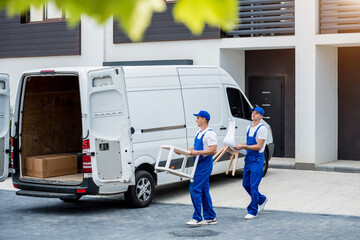 Two removal company workers are loading boxes and furniture into a minibus.