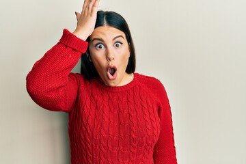 Beautiful brunette woman wearing wool winter sweater surprised with hand on head for mistake,...