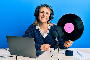 Young caucasian woman working at radio studio holding vinyl disc looking positive and happy standing and smiling with a confident smile showing teeth