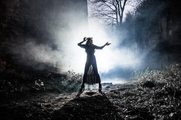 A young witch dances and conjures on Halloween night in smoke and light at the festival of the dead.